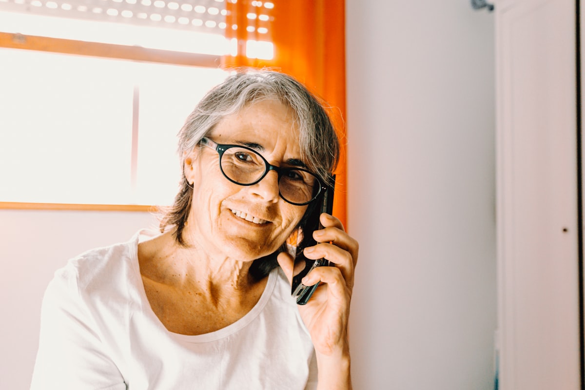 Une femme âgée souriante qui parle au téléphone chez elle